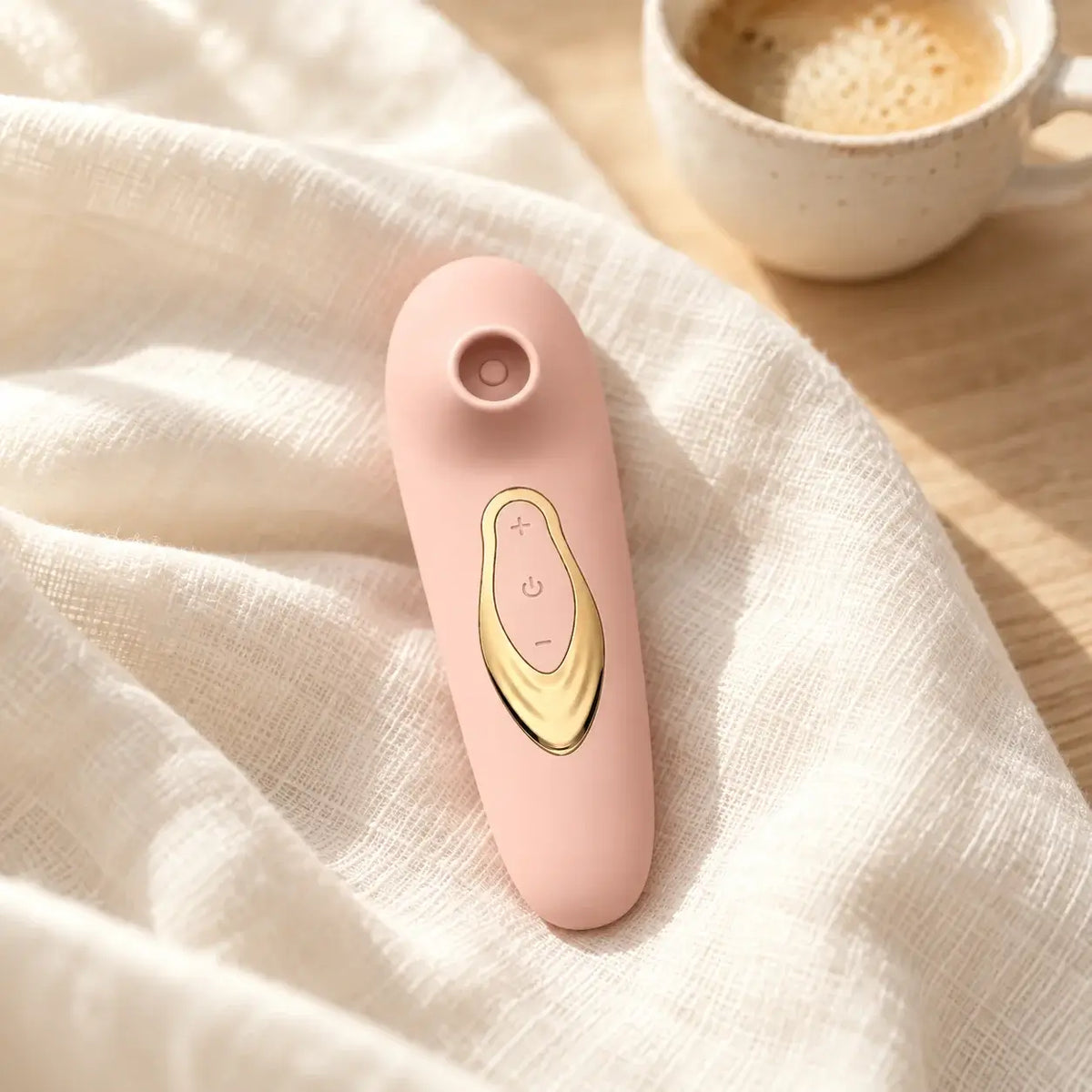 Stimulateur Halo rose poudré posé sur un drap en lin, à côté d’une tasse de café
